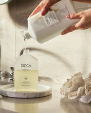 Oceanique Hand Wash being poured from a refill bottle into a pump bottle beside a basin.