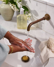 White Tea & Wild Mint Hand Wash styled beside a basin while hands are washed.