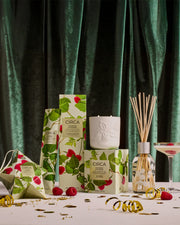 Raspberry & Rhubarb candles, diffuser and festive gift packaging styled with green curtains and Christmas decorations.