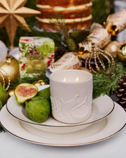White Fig & Cedar candle burning in its embossed fig vessel on a festive place setting with fresh figs.